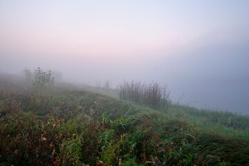Foggy dawn on the field near the lake.