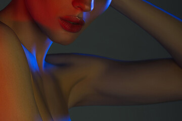 Lips, collarbones and shoulder of young beautiful woman in neon light closeup