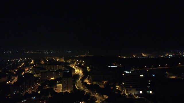 Vista a&eacute;rea noturna da cidade capturada por drone, destacando arranha-c&eacute;us iluminados e as luzes movimentadas das ruas abaixo
