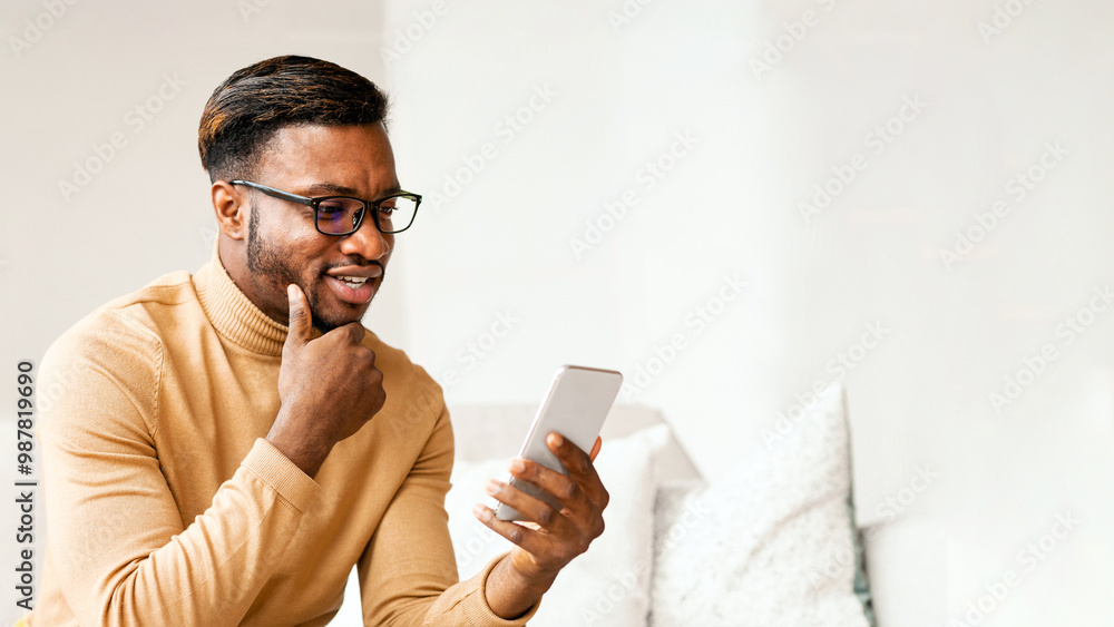 Poster modern communication. positive afro man using cellphone texting sitting on sofa at home. copy space