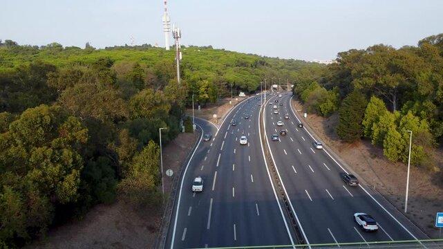 Autoestrada em Monsanto, Lisboa, ao p&ocirc;r do sol com tr&aacute;fego em movimento. O c&eacute;u alaranjado ilumina a estrada e os ve&iacute;culos, criando um contraste entre a natureza e a paisagem urbana.