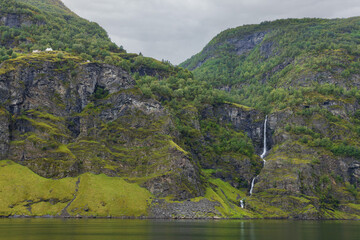 The mountainous landscape of Flam towers over the fjords of Aurlandsfjord and Naeroyfjord with many waterfalls from the towering cliffs, Norway.