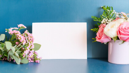 Charming bouquet of roses with vibrant greenery and blank white note card against blue backdrop.