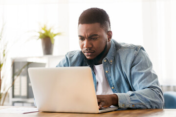Important task. Focused african american employee working on laptop in office, free space