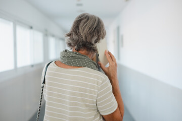 Back view of senior Caucasian woman walking in a corridor of a building while using the phone....