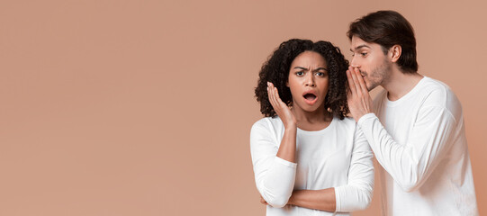 Unexpected news. Young man gossiping with his afro girlfriend, whispering secret to her ear,...