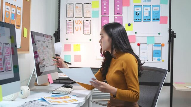 Female ux designer analyzing mobile app interface wireframe designs on a computer in an office. She is working on a user experience for a new website