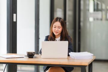 Focused Businesswoman at Work: A professional woman in a suit concentrates on her laptop, surrounded by paperwork and a cup of coffee, representing dedication, productivity, and success in the modern 