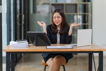 Engaged in Digital Dialogue: A young Asian businesswoman, seated at her modern office desk, gestures expressively during a video conference call on her tablet.