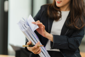 Businesswoman Organizing Documents: A young Asian professional in a sleek black suit meticulously...