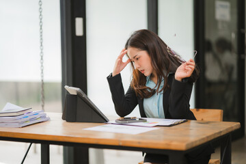 Overwhelmed Businesswoman:  A young Asian businesswoman grapples with stress at her desk, her hand on her head, reflecting the pressures of the modern workplace.