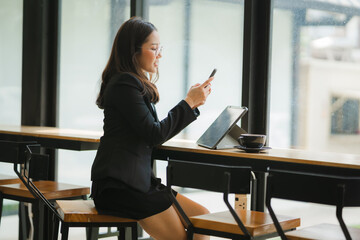 Businesswoman Working on Tablet in Cafe: A professional woman in a stylish black blazer and skirt,...