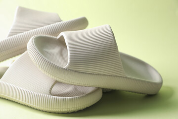 Three white rubber slippers on green background, closeup