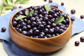 Ripe acai berries and leaves in bowl on grey table, closeup