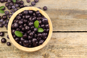 Ripe acai berries and leaves in bowl on wooden table, top view. Space for text