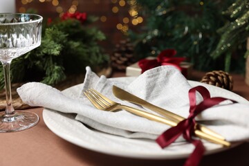 Christmas place setting with plate, napkin, cutlery and festive decor on brown table, closeup