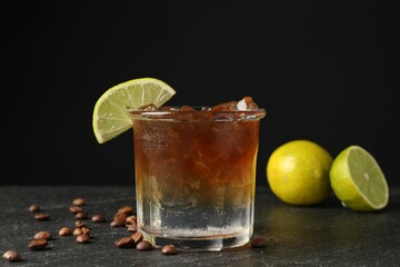 Refreshing espresso tonic drink with slice of lime and coffee beans on dark table, closeup
