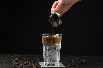 Woman making refreshing espresso tonic drink at dark table, closeup