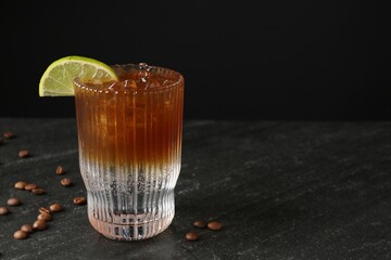 Refreshing espresso tonic drink with slice of lime and coffee beans on dark table. Space for text