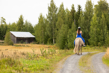 Lady with blue dress riding on Icelandic horse during sunset in Finland. Rider is wearing helmet.