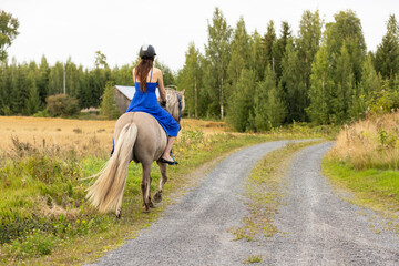 Lady with blue dress riding on Icelandic horse during sunset in Finland. Rider is wearing helmet.