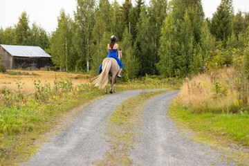 Lady with blue dress riding on Icelandic horse during sunset in Finland. Rider is wearing helmet.