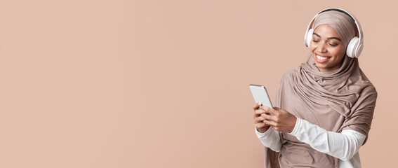 Cool music app. Smiling black muslim girl in hijab listening her favorite songs with wireless...