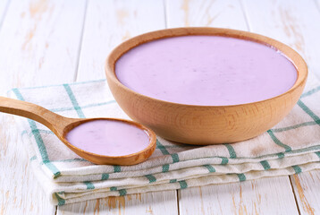 blueberry smoothie in a wooden bowl with spoon on a white table, selective focus.