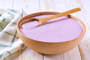 blueberry smoothie in a wooden bowl with spoon on a white table, selective focus.