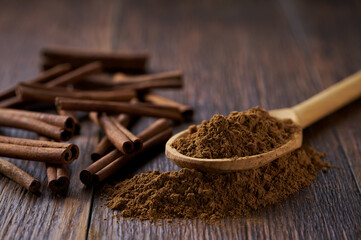 cinnamon powder poured out of a wooden spoon on a dark wooden table, selective focus.