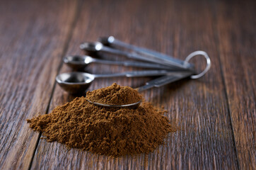 cinnamon powder poured out of a measuring spoon on a dark wooden table, selective focus.