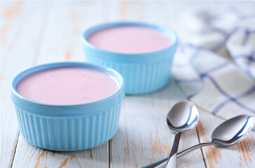 pink fruit yogurt in a ceramic bowl with spoon on a light background, selective focus.