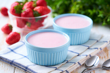 pink fruit yogurt in a ceramic bowl with with fresh strawberry on a light background, selective focus.