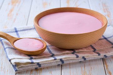 strawberry smoothie in a wooden bowl with spoon on a white table, selective focus.