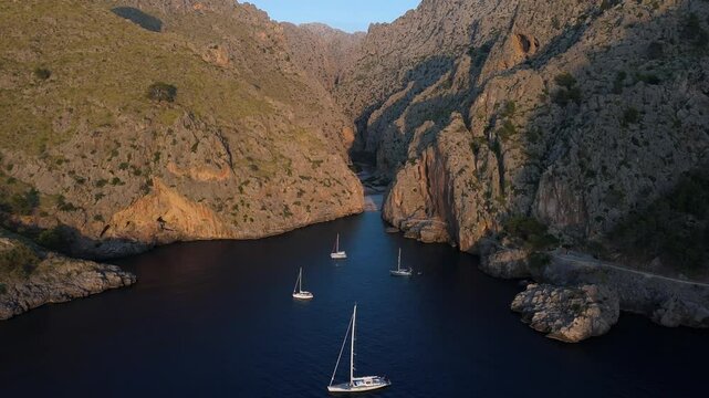 Aerial of yachts in Sa Calobra bay with rocky mountain coast at sunset, Mallorca