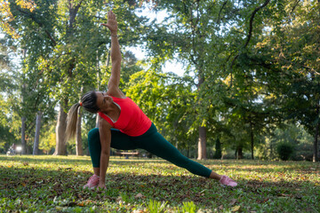 Athlete doing stretching exercises in city park. Woman runner stretching leg muscles by touching his shoes and looking away. Fitness and lifestyle concept. Mature sports woman stretching muscles 