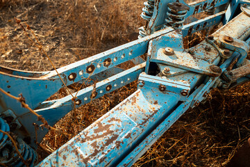 A close-up of a rusty, blue metal structure with bolts and components, set against a dry, grassy background.