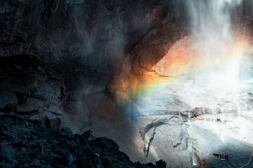 A waterfall cascades down, its mist catching the sunlight and creating a vibrant rainbow that arches gracefully across the rushing water.