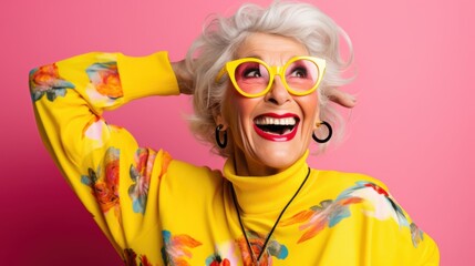A senior woman with a vibrant sweater and quirky glasses, laughs joyfully against a bright pink background, showcasing her lively spirit.