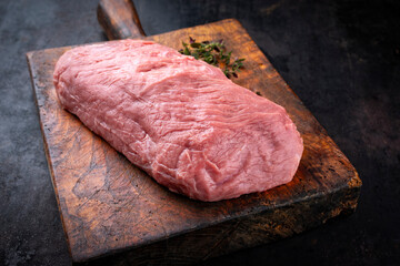 Raw veal steak decorated with herbs offered as close-up on an old rustic wooden cutting board with...