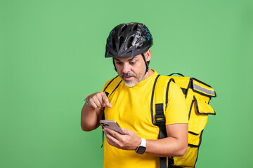 Delivery man checking smartphone while on green screen background, wearing yellow uniform.
