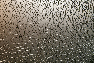 Shattered safety glass illuminated from the side against a calm background with a pattern similar...