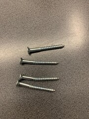 Four screws on a dark grey background, two of which are slightly bent and one severely bent, show...