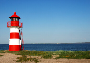 Fototapeta premium Ein kleiner Mini Leuchtturm steht am Ufer der Ostsee zwischen Sand und Seegras bzw. Schilf vor blauem Himmel und der weiten See im Horizont