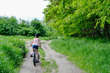 Fototapeta premium Young girl cyclist enjoy the beautiful sunrise on summer forest trail. Close-up portrait of a happy little girl in a helmet on a bicycle. High quality photo