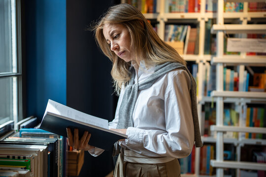 Passionate woman reviews and picks books from bookshelves in bookstore or library. Female reading enthusiast on book fair, book sales, library visit, book exchange, literature lover, bookworm