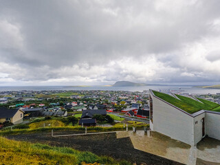 Fototapeta premium Aerial views looking out over the Capital city of the Faroe Islands, Tórshavn. The North Atlantic Ocean and the small remote island of Nolsoy can be seen in the distance. Streymoy, Faeroe Islands.