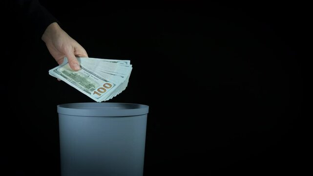 Lady hand throw money away. A view of lady hand with money put in into the plastic trash on black background.
