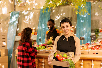 Smiling female vendor posing next to farmers market stand, showcasing healthy food natural products...