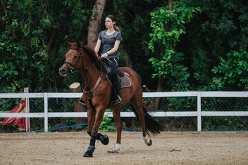 A girl rides a brown horse in an outdoor ranch setting, with lush green trees in the background.